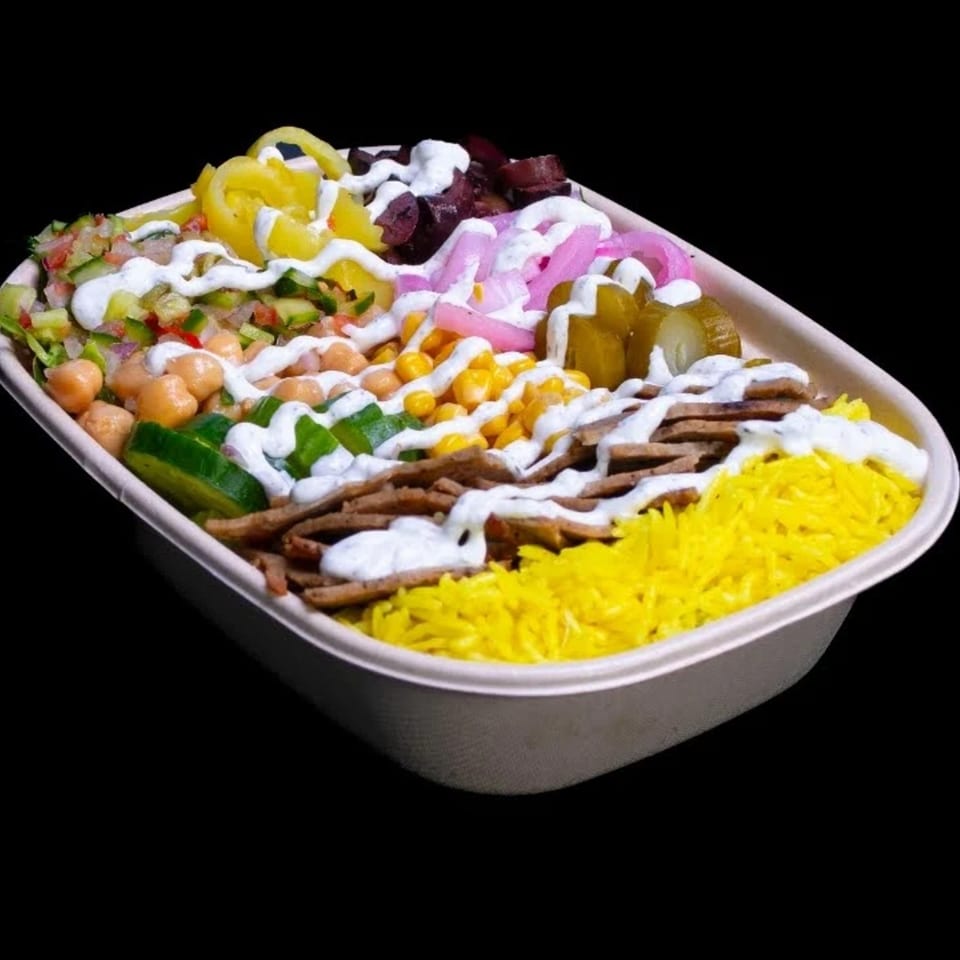 A colorful Build-A-Pita & Pizza bowl with yellow rice, meat, chickpeas, corn, and various pickled vegetables.