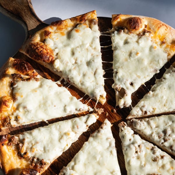 Build-A-Pita & Pizza Restaurant's sliced pizza with melted cheese and meat on a wooden board.