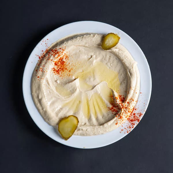 Creamy hummus drizzled with olive oil, sprinkled with paprika, and garnished with pickle slices.