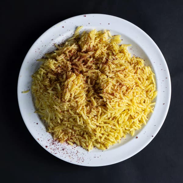 A white plate filled with yellow seasoned rice, sprinkled with red spices, on a dark background.